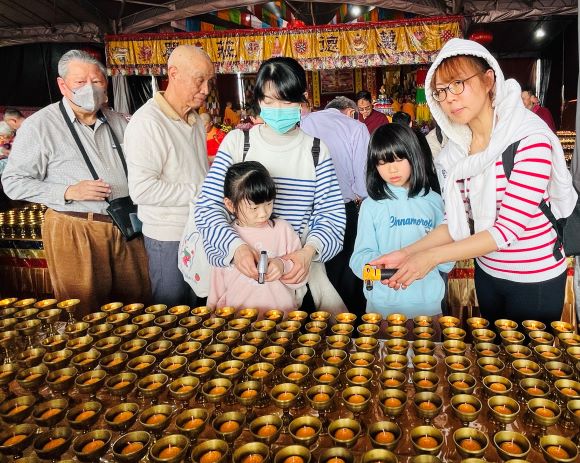 《圖說》2026新春萬燈供佛法會，媽媽帶著小孩子同沾法喜點燈祈求吉祥光明。〈主辦單位提供〉