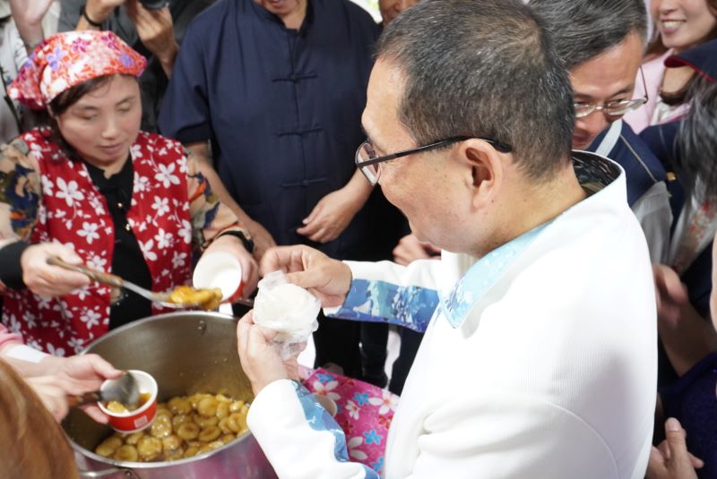 《圖說》侯友宜市長在活動現場的美食區與鄉親話家常，並品嚐客家菜包，氣氛熱鬧、溫馨。〈客家局提供〉